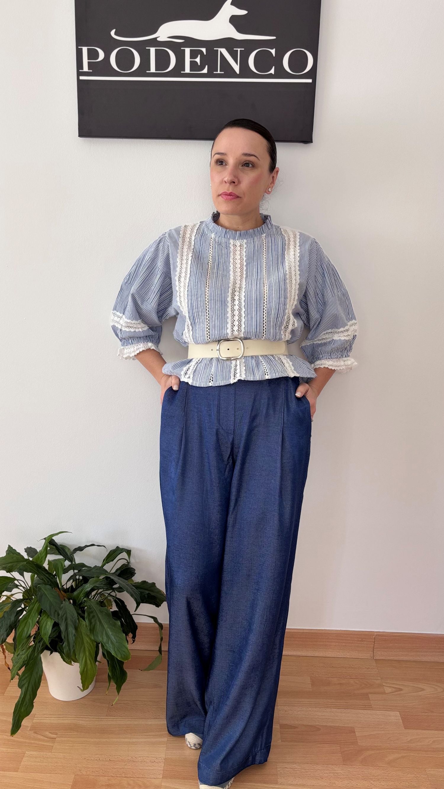 Mujer con la Blusa Ana de rayas verticales azul y blanca, mangas abullonadas y detalle de encaje, posando con estilo relajado y elegante.