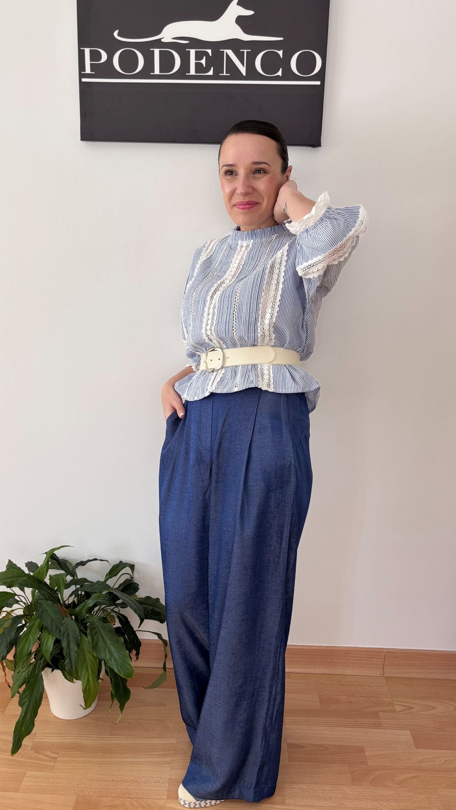 Mujer con la Blusa Ana de rayas verticales azul y blanca, mangas abullonadas y detalle de encaje, posando con estilo relajado y elegante.