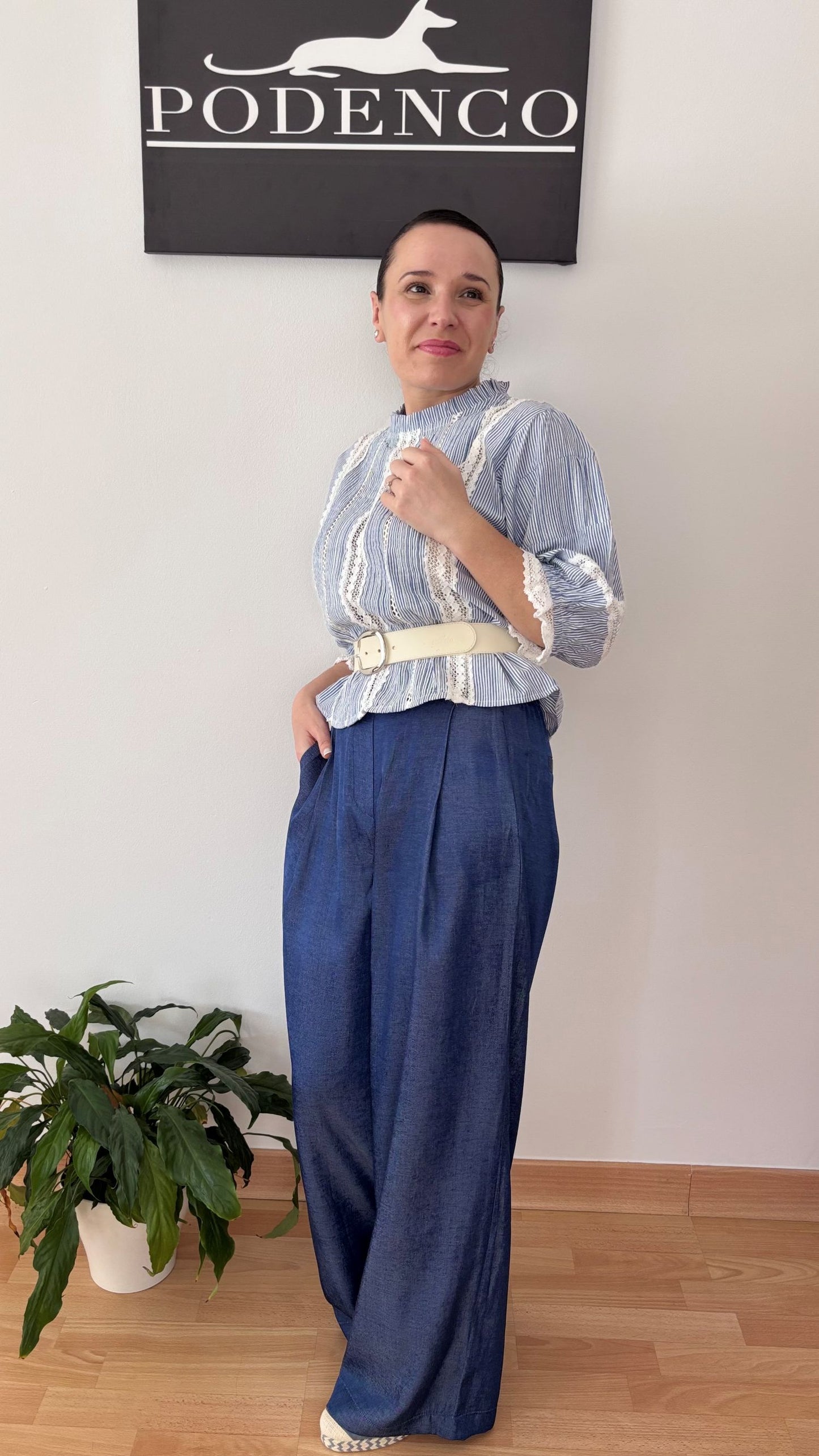 Mujer con la Blusa Ana de rayas verticales azul y blanca, mangas abullonadas y detalle de encaje, posando con estilo relajado y elegante.