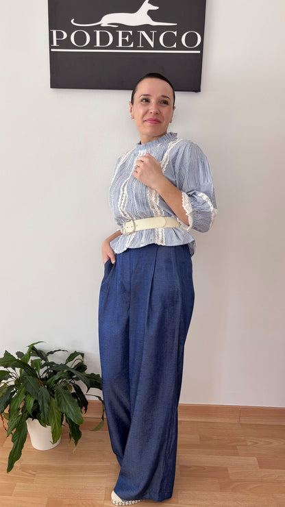 Mujer con la Blusa Ana de rayas verticales azul y blanca, mangas abullonadas y detalle de encaje, posando con estilo relajado y elegante.